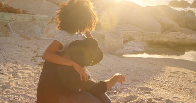 Romantic diverse couple sitting and embracing on beach at sunrise. Summer, vacation, romance, love, relationship, free time and lifestyle, unaltered.