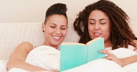 Happy Women Sharing Book in Cozy Bed with Joyful Laughter