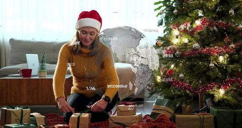 Woman tying ribbons on christmas gifts by decorated tree with augmented reality globe