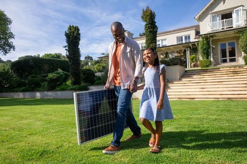 Father and Daughter Carrying Solar Panel at Green Suburban Home