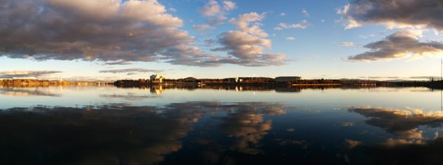Panoramic view showing serene sunset over calm lake with clear reflections of clouds and sky. Ideal for use in travel promotions, nature magazines, stock images for websites, backgrounds for slideshows, or inspirational content.