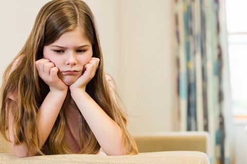 Reflective Girl Resting Chin on Sofa at Home by Patterned Curtains