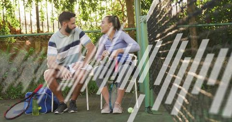 Sunlit tennis break: chatting friends sitting on court chairs with rackets and gear