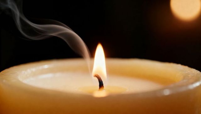 Pillar candle burning with flickering flame and curling smoke plume in warm low light