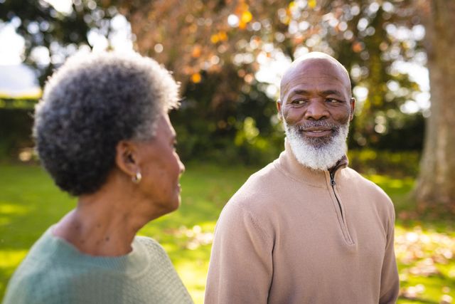 This image depicts a senior African American couple standing in a park during winter, looking at each other with affection. It is perfect for use in advertisements, brochures, and articles related to retirement, senior living, relationships, and outdoor activities. It can also be used in healthcare and wellness promotions focusing on elderly well-being and active lifestyles.