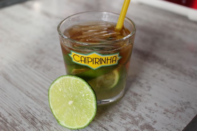 Caipirinha cocktail with lime slices and ice in glass on wooden table. Perfect for promoting summer drinks, tropical parties, cocktail bars, and refreshing beverages.