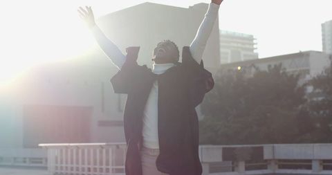 Young man raising arms to sunrise on rooftop celebrating freedom and urban joy