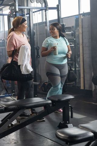 Diverse female friends chatting after gym workout with duffel bag and protein shaker