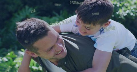 Smiling father carrying son piggyback in sunlit garden with playful data overlay