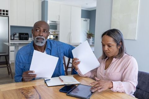 Senior couple reviewing finances on tablet and paperwork at modern kitchen table