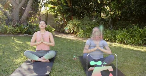Sunlit garden yoga: two women meditating on mats with digital wellness app overlay
