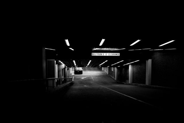 This image captures an empty underground parking garage at night with minimal lighting, providing a moody and eerie atmosphere. Ideal for illustrating concepts of isolation, urban life, and clandestine activities. Suitable for use in thriller visuals, urban studies, or as a background for topics on transportation facilities.