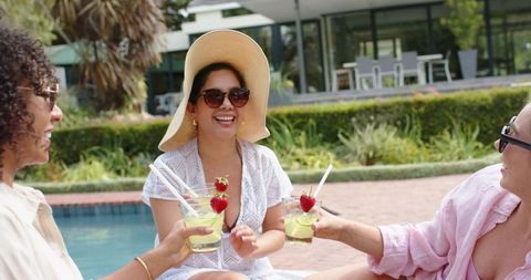 Multiracial women laughing and enjoying cocktails by poolside at resort patio
