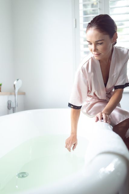 Woman in a modern bathroom preparing a bath, ideal for concepts of self-care, relaxation, and home wellness. Suitable for advertisements, blogs, or articles related to home living, personal care routines, and interior design.