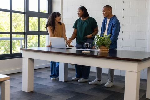 Diverse coworkers collaborating and brainstorming around laptop in modern bright workspace