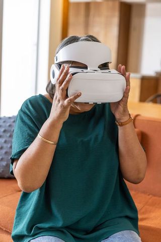 Senior Asian Woman Using VR Headset in Living Room for Leisure