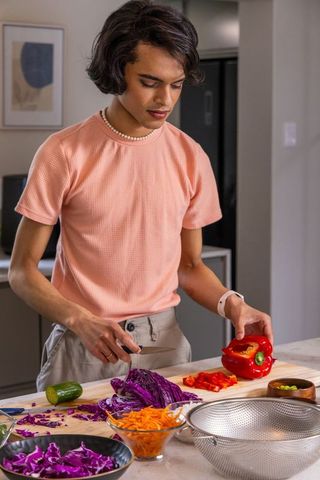 Indian man chopping red bell pepper on kitchen island preparing colorful vegetable salad