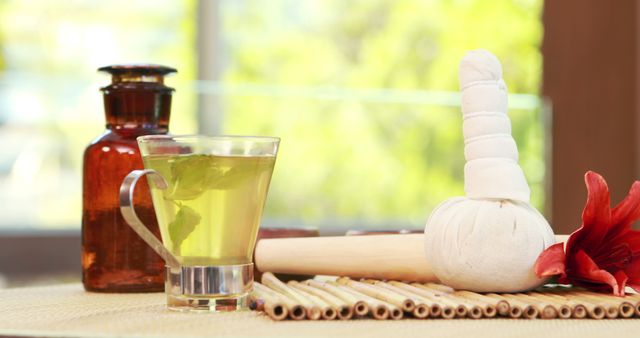 A serene spa setting features a cup of herbal tea, massage oils, and a herbal compress, with copy space. These elements are commonly used in wellness and relaxation therapies to promote healing and tranquility.