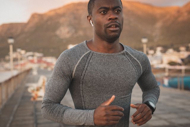 African American man running on a pier at sunset, showcasing a healthy outdoor lifestyle. Ideal for use in fitness, health, and wellness promotions, as well as advertisements for sportswear, exercise equipment, and motivational content.