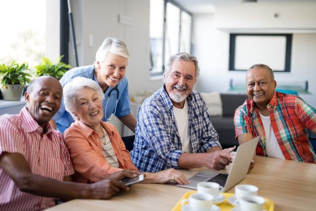 Group of happy seniors with a caregiver gathered around a table, using a laptop. Ideal for illustrating senior living, healthcare, technology use among the elderly, and community support in retirement homes. Perfect for websites, brochures, and articles related to elderly care, senior activities, and nursing home environments.