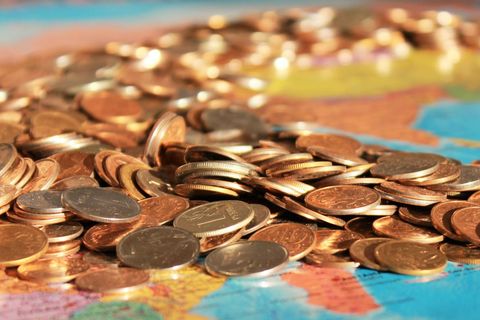 Spilling copper coins over colorful world map representing global travel finance concept