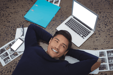 Relaxed businessman lying near transparent laptop with photo prints