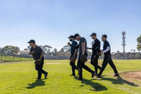 Adult baseball team walking across sunlit field carrying gloves and caps, showing teamwork