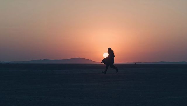 Leaping woman silhouette at sunset on vast plain wearing long coat and boots
