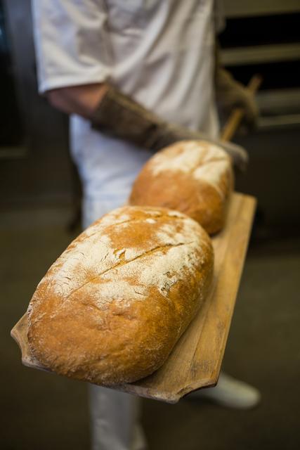 Baker removing freshly baked bread loaves from oven using wooden peel, highlighting artisan bread-making process. Ideal for use in articles, advertisements, or content related to baking, culinary skills, artisanal bread, professional kitchens, or homemade food.