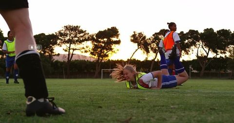 Blonde Female Soccer Player Falling and Grimacing During Sunset Practice on Grass Field