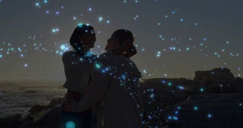 Romantic Couple Embracing on Rocky Coast at Sunset Silhouette with Glowing Particles and Bokeh