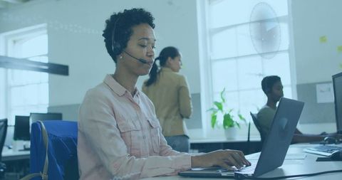 Typing customer support agent wearing headset in modern open-plan office