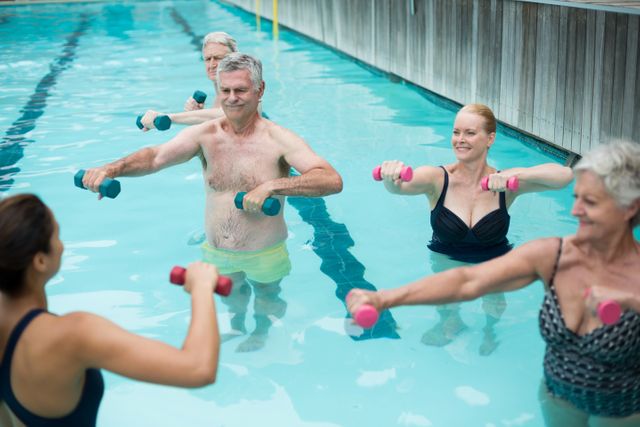 Group of senior individuals participating in a water aerobics class, lifting dumbbells under the guidance of an instructor. Ideal for promoting senior fitness, health and wellness programs, aquatic exercise classes, and active lifestyle for elderly people.