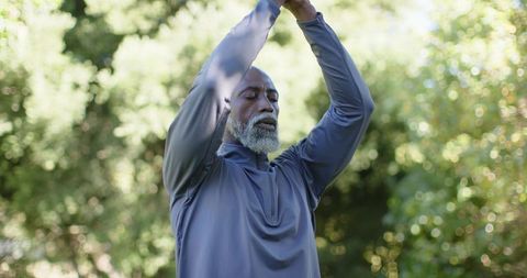 Senior african american man practicing mindful overhead stretch in sunlit park