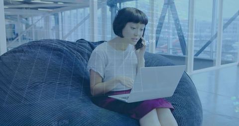 Remote worker balancing laptop and phone in modern coworking lounge with data overlay