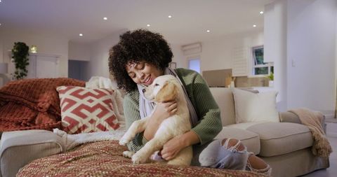 Young woman cuddling golden retriever puppy on cozy sofa in open-plan living room