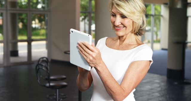 A senior Caucasian woman is engaged with a tablet, smiling as she navigates the device, with copy space. Her comfort with modern technology reflects the increasing digital literacy among older generations.