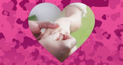 Placing engagement ring during romantic garden proposal with heart cutout and pink bokeh