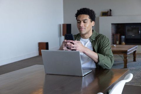 African American Male Using Smartphone and Laptop at Home