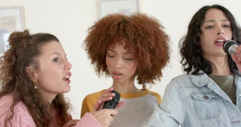 Diverse women singing together holding microphones living room rehearsal casual harmony