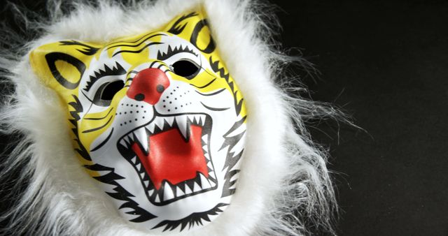 A colorful tiger mask with faux fur is displayed against a black background, with copy space. Masks like this are often used in costumes for parties, theatrical performances, or festive celebrations.