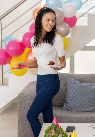 Smiling teenage girl holding cake and macaron, celebrating birthday with colorful balloons