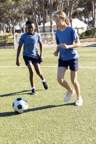 School children playing soccer on turf during outdoor pe showing teamwork and diversity