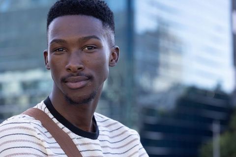 Stylish african american man smiling in city headshot wearing striped sweater and strap