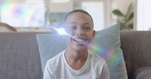 Smiling boy relaxing on sofa with rainbow lens flare in bright modern living room
