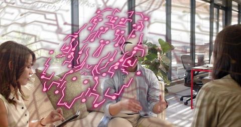 Man wearing vr headset gesturing with neon brain overlay, team collaborating in office lounge