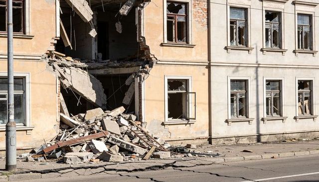 Collapsed building facade with rubble pile and exposed floor slabs on urban street