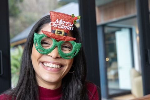 Smiling woman wearing festive green glitter glasses with red mini christmas hat