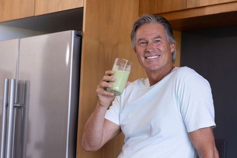 Healthy senior man enjoying green smoothie in modern kitchen, smiling, wellness lifestyle