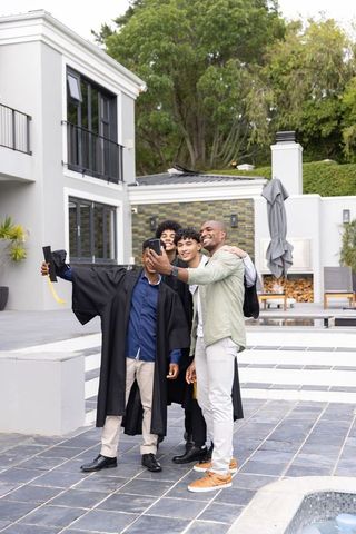Graduates taking selfie with family on modern backyard poolside patio